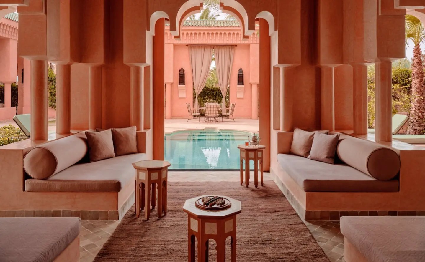 Blick aus dem schattigen Salon einer Pool Villa durch maurische Bögen auf den privaten Pool und den Gartenpavillon