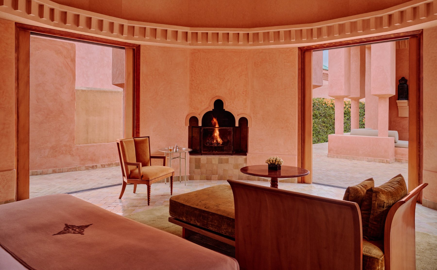 Salon eines Pavillons in Amanjena mit offenem Kamin, weit geöffneten Türen zum Innenhof, Samtdaybed und Minztee auf einem kleinen Tisch
