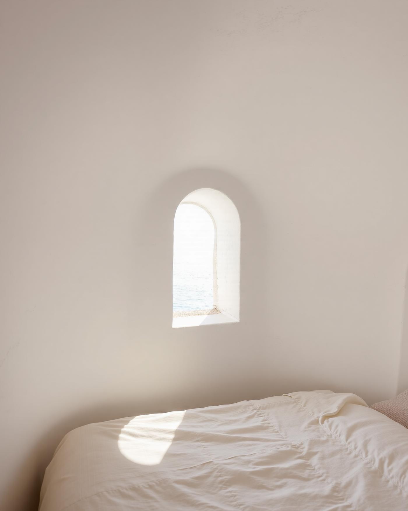 A minimal Cycladic bedroom with curved white plaster walls and a small arched sea window
