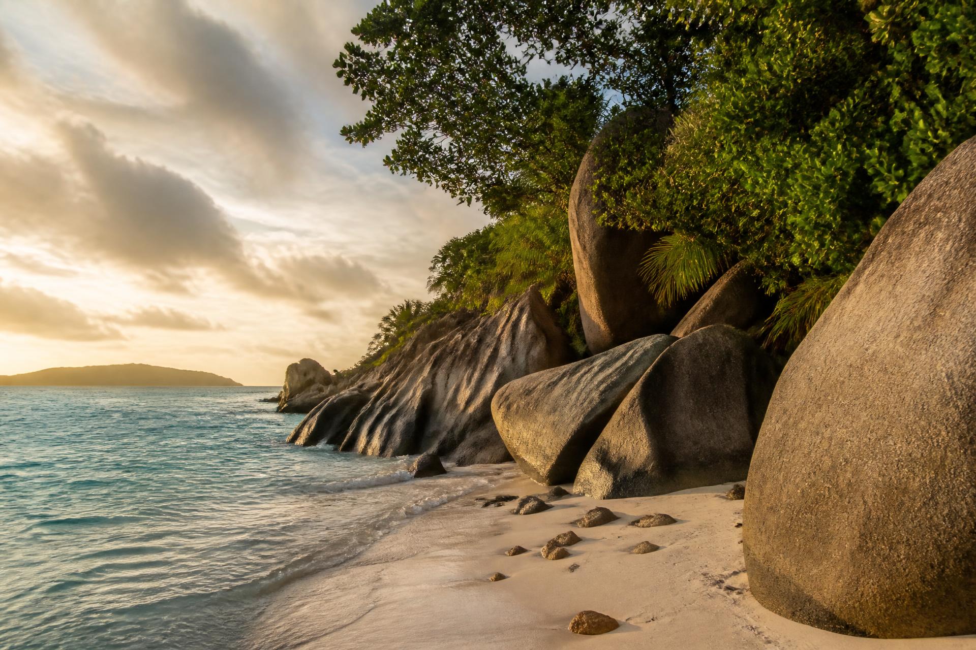 Granite boulders on a Seychelles beach with turquoise water and takamaka trees at dusk