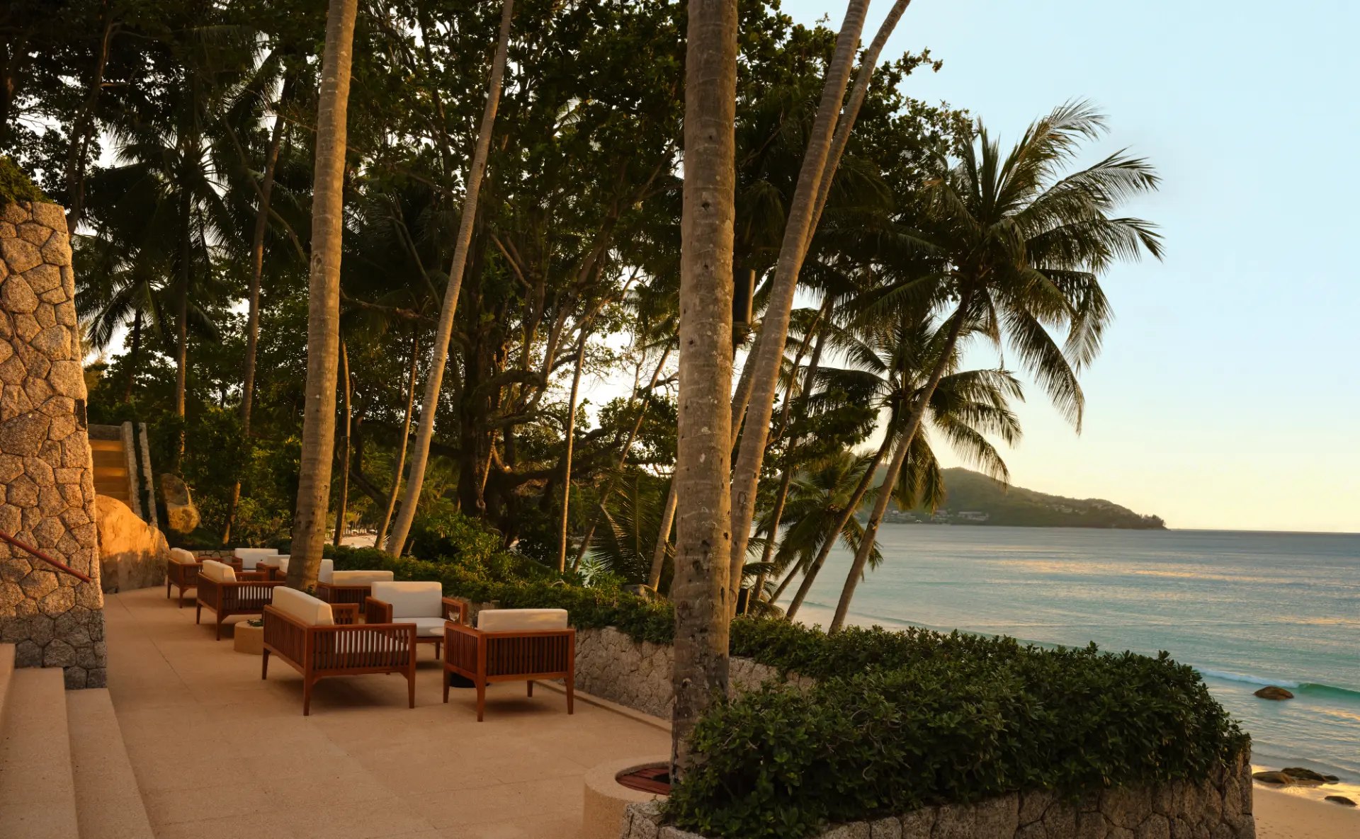 Sitzgruppen auf der Sunset Terrace zwischen Kokospalmen, dahinter das Meer im späten Nachmittagslicht