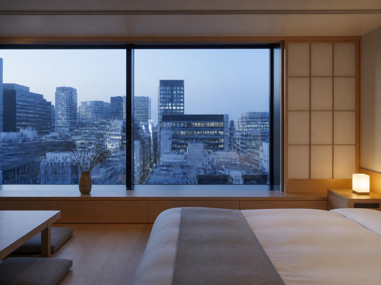 Minimalist Tokyo hotel room with floor to ceiling window over rooftops at blue hour, pale wood and washi paper screen