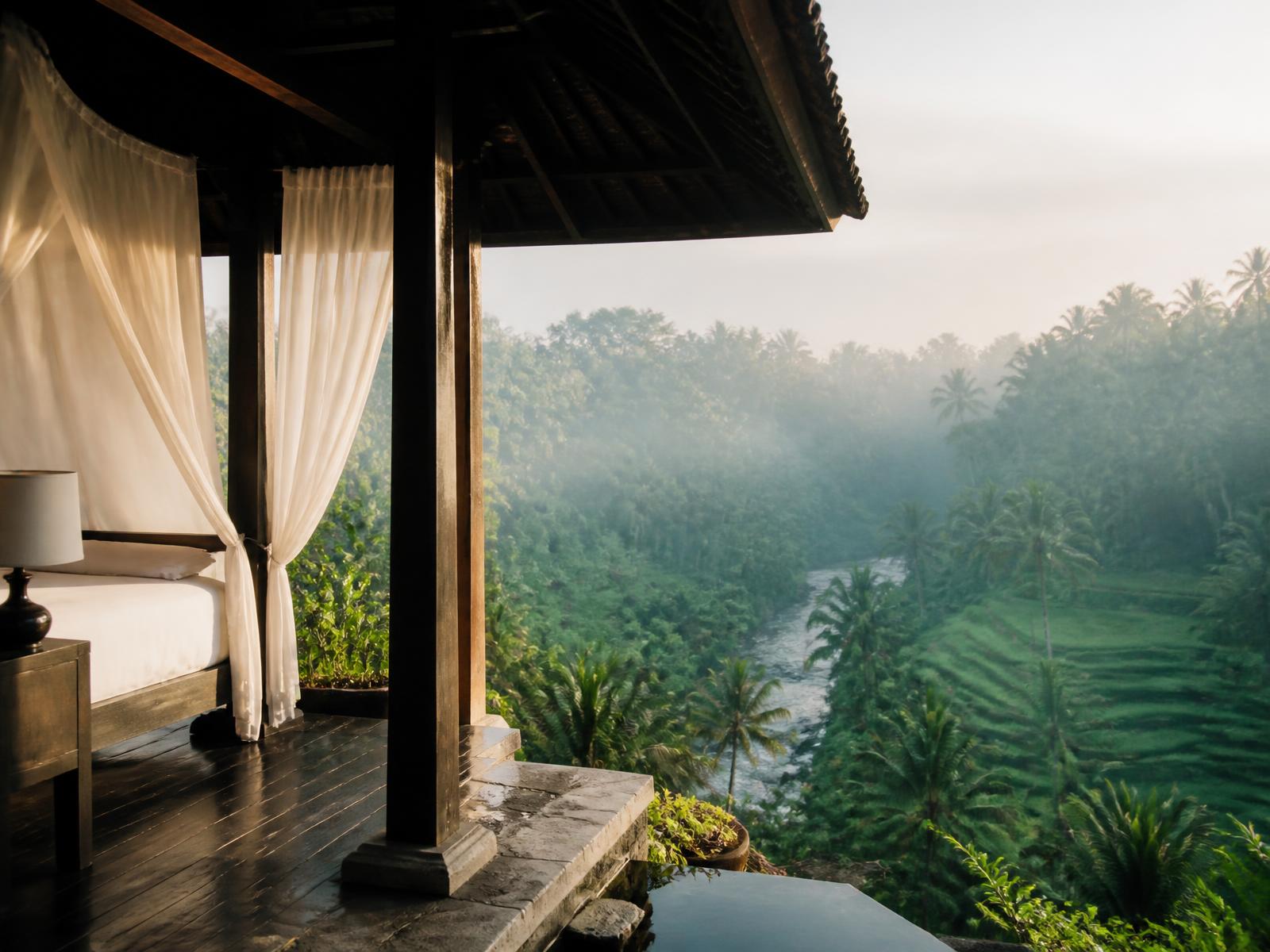 Dark timber Balinese pavilion with white linen overlooking a misted jungle river valley