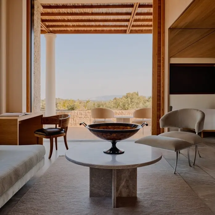 Sitzbereich einer Amanzoe-Villa mit rundem Steintisch, Sessel und offener Front zu Säulen, Pergola und Hügeln