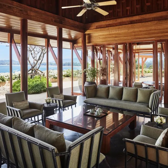 Offener Wohnraum einer Villa mit Teakstützen, tiefen Sofas und Blick über die Bucht