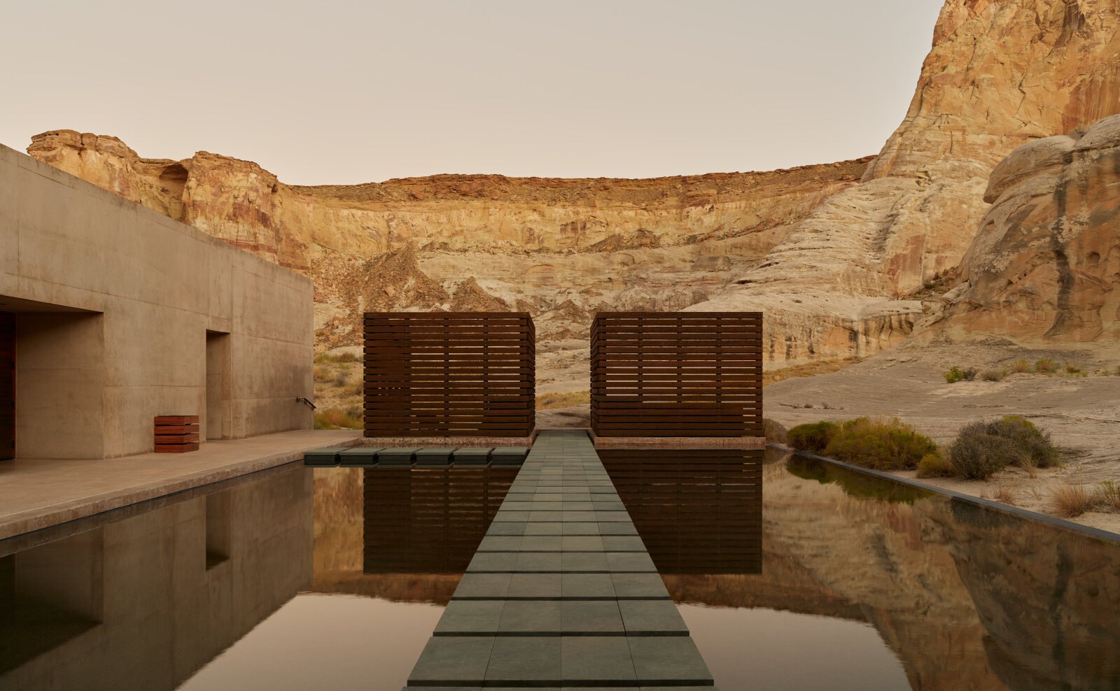 Das Aman Spa in Amangiri: ein spiegelglattes Wasserbecken mit steinernem Steg zwischen zwei hölzernen Lamellenpavillons, dahinter die Felswände des Canyons