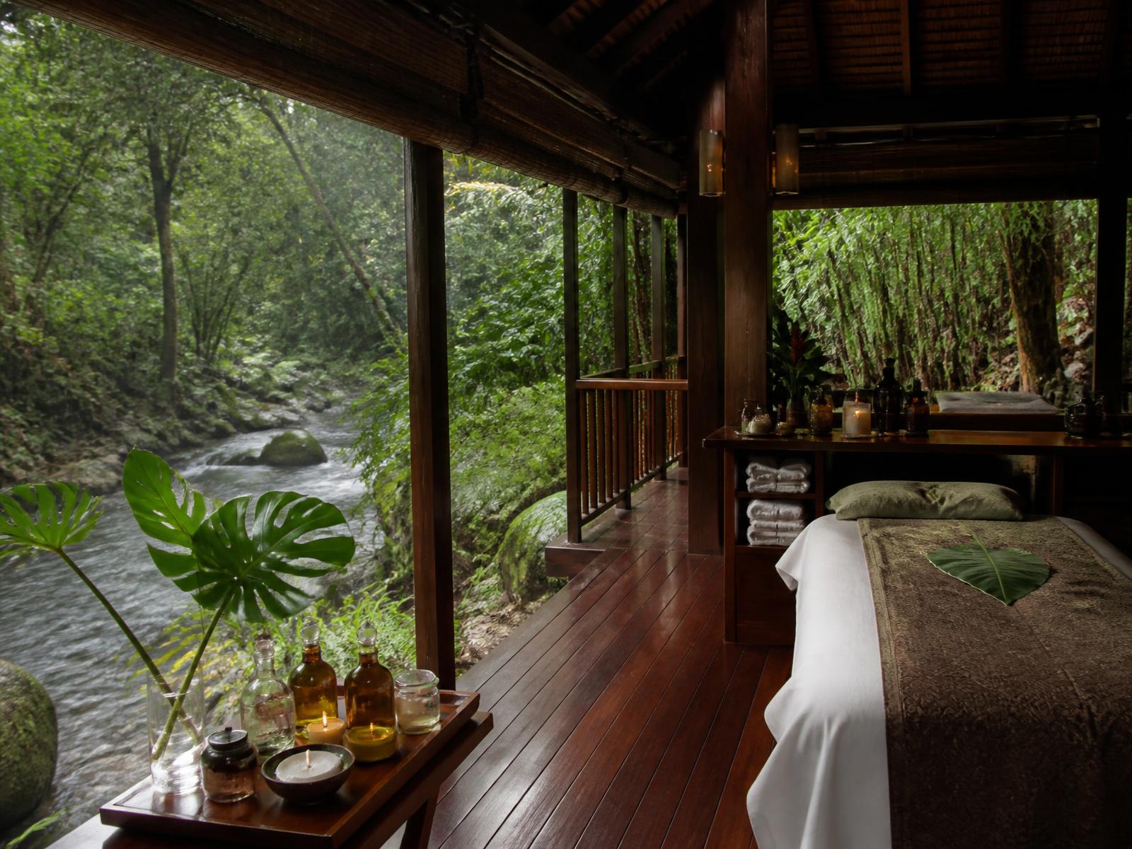 Open timber spa pavilion above a natural jungle stream in Malaysian rainforest with folded linen and botanical oils