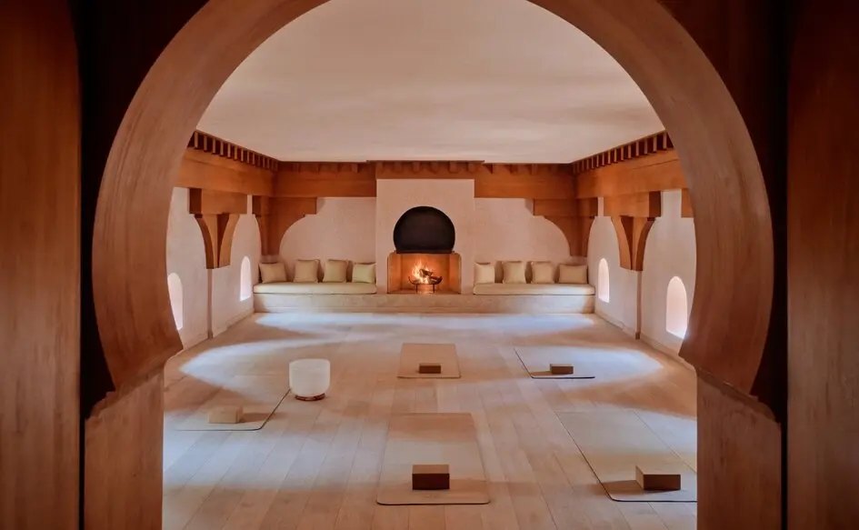 Das Yoga-Studio von Amanjena hinter einem Hufeisenbogen: heller Holzboden, Matten, gepolsterte Bank und offenes Kaminfeuer