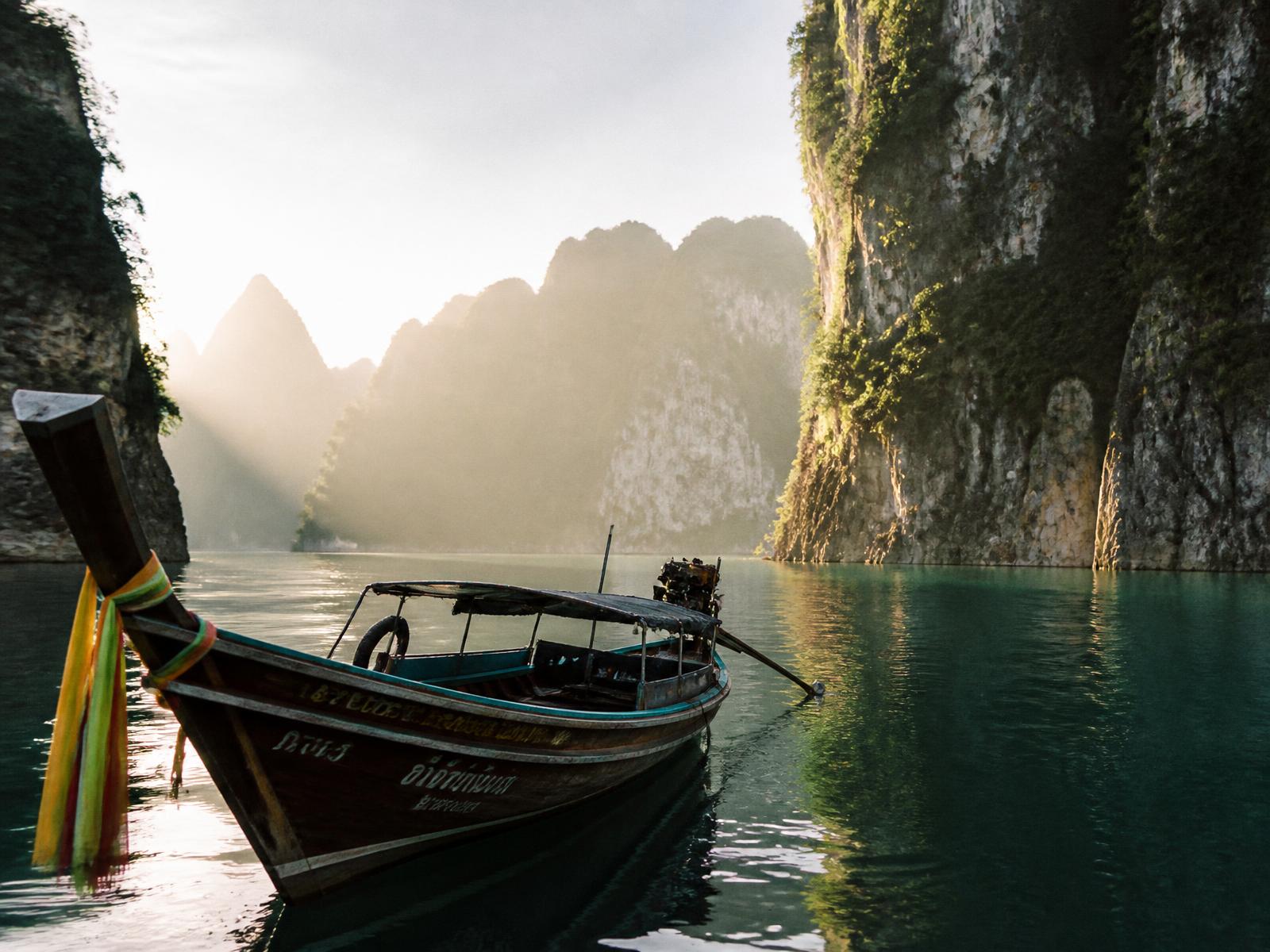 Limestone karst islands rising from a still emerald bay with a wooden longtail boat in morning mist