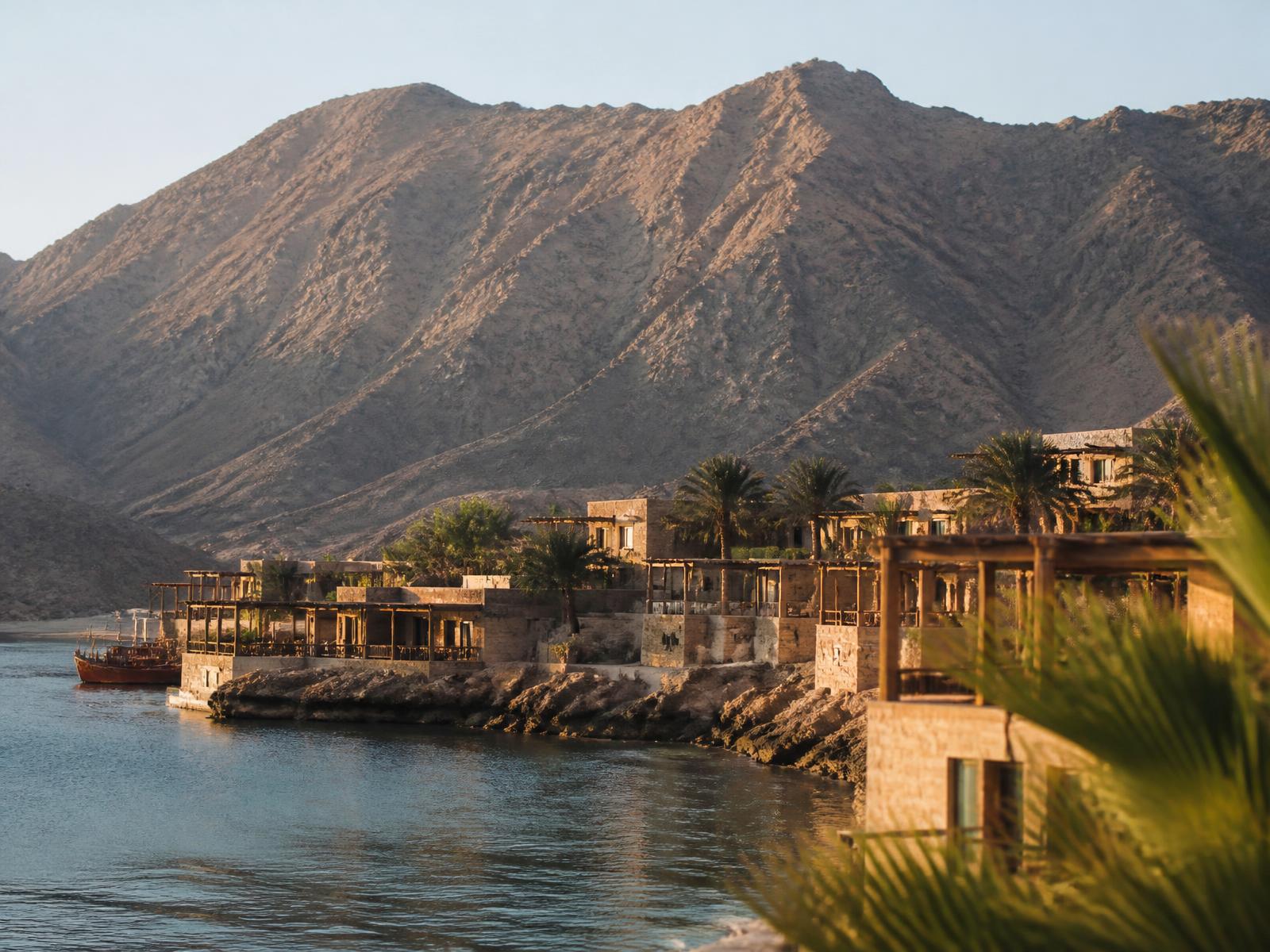 Stone flat-roofed villas in the style of an Omani fishing village at the foot of bare mountains beside a calm bay